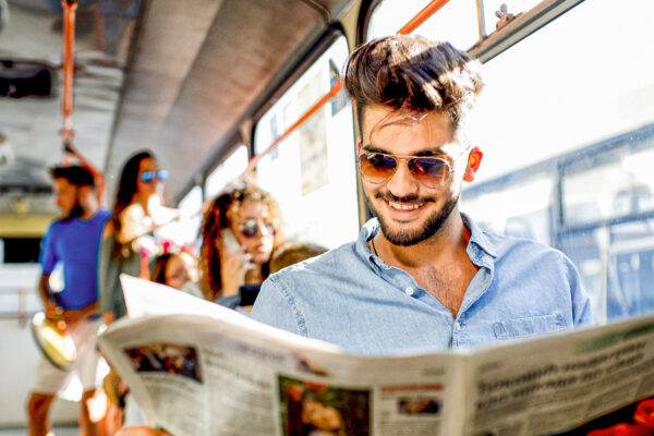 The busy businessman sits in the bus and reads the newspapers.