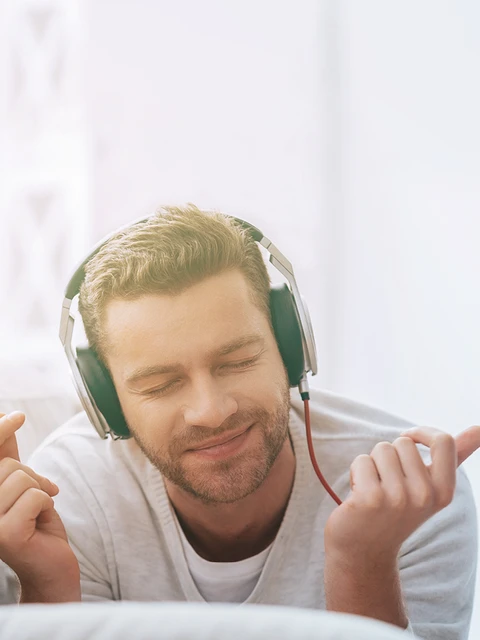 Mann liegt auf Sofa und hört happy Musik mit Kopfhörern.