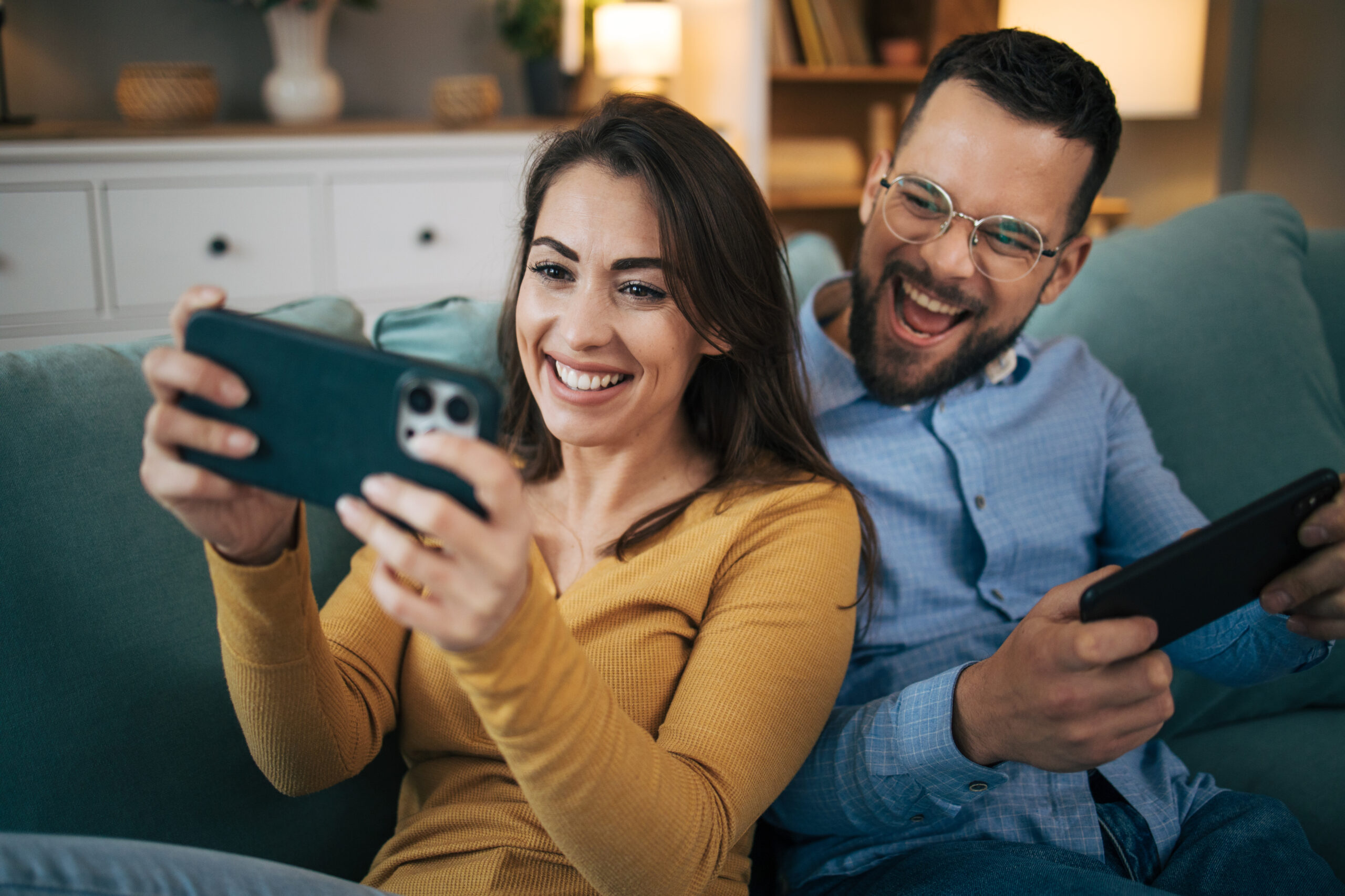 Shot of a young couple lounging at home in the living room playing games on their cell phone.