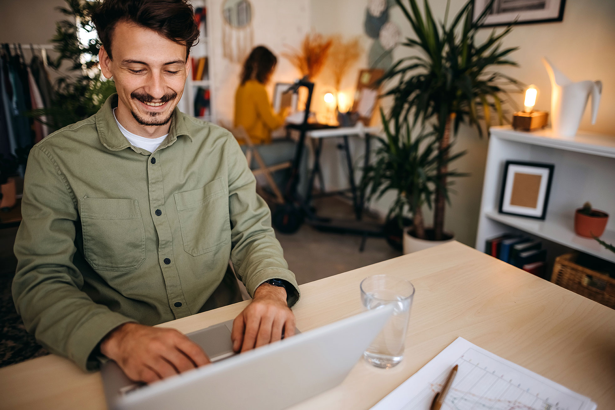 Junger Mann sitzt vor einem Laptop in einer sehr gemütlichen Agentur und arbeitet zufrieden.